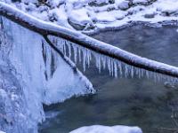 Eiszapfen hängen an querliegendem Stamm über dem Bach